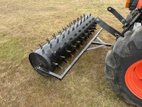 Tractor-mounted spiked roller aerator on a grass pasture