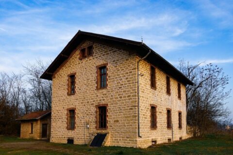 Traditional stone farmhouse with shuttered windows beside leafless trees