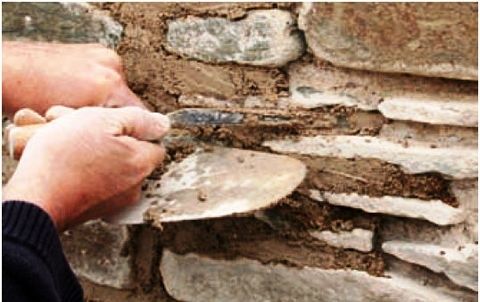 Hands applying mortar between stones in an old masonry wall